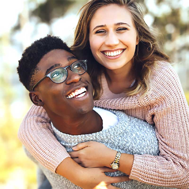 A boy with glasses giving a girl in a pink sweater a piggy back ride