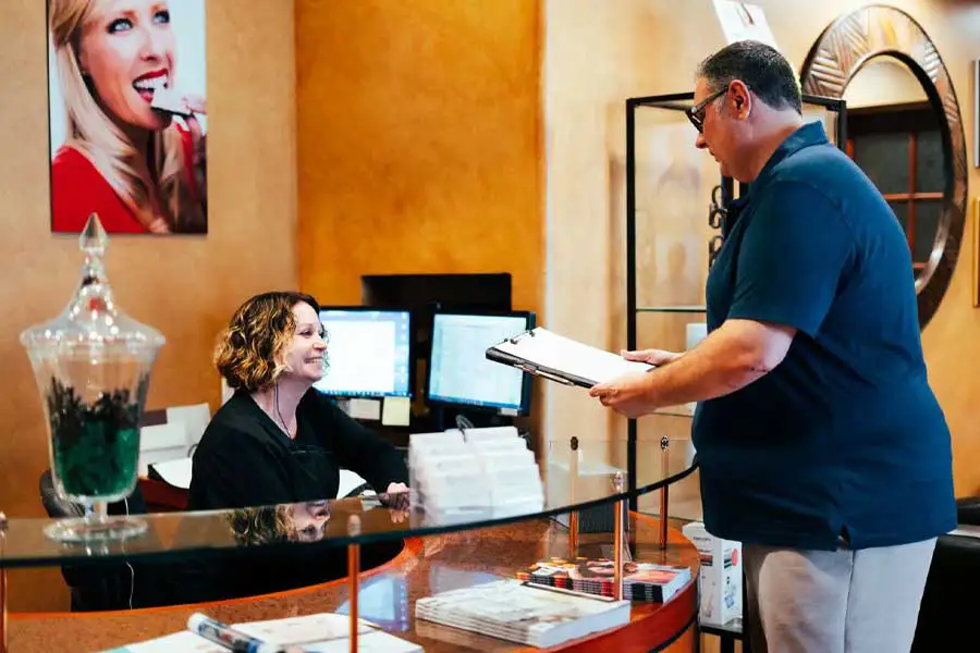 A patient standing at the front desk with paperwork at GOREgeous Smiles