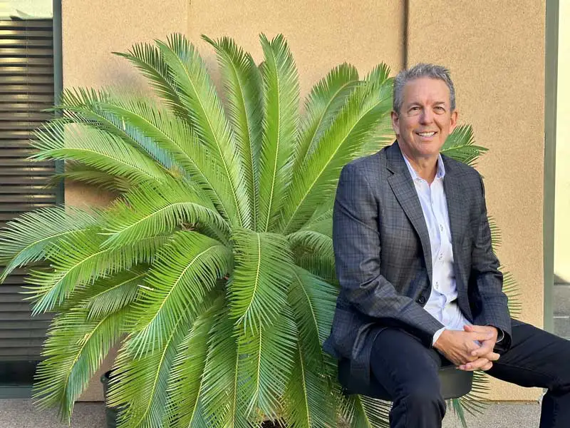 Dr. Gore sitting and smiling with a palm tree in the background at GOREgeous Smiles 