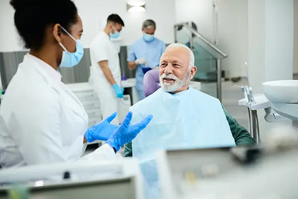 Older patient sitting in dental chair calmly discussing his oral health with his dentist