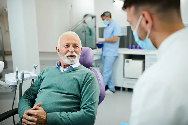 An older male patient sitting in a dental chair and consulting with a dentist in a modern clinic. An older male patient sitting in a dental chair and consulting with a dentist in a modern clinic.